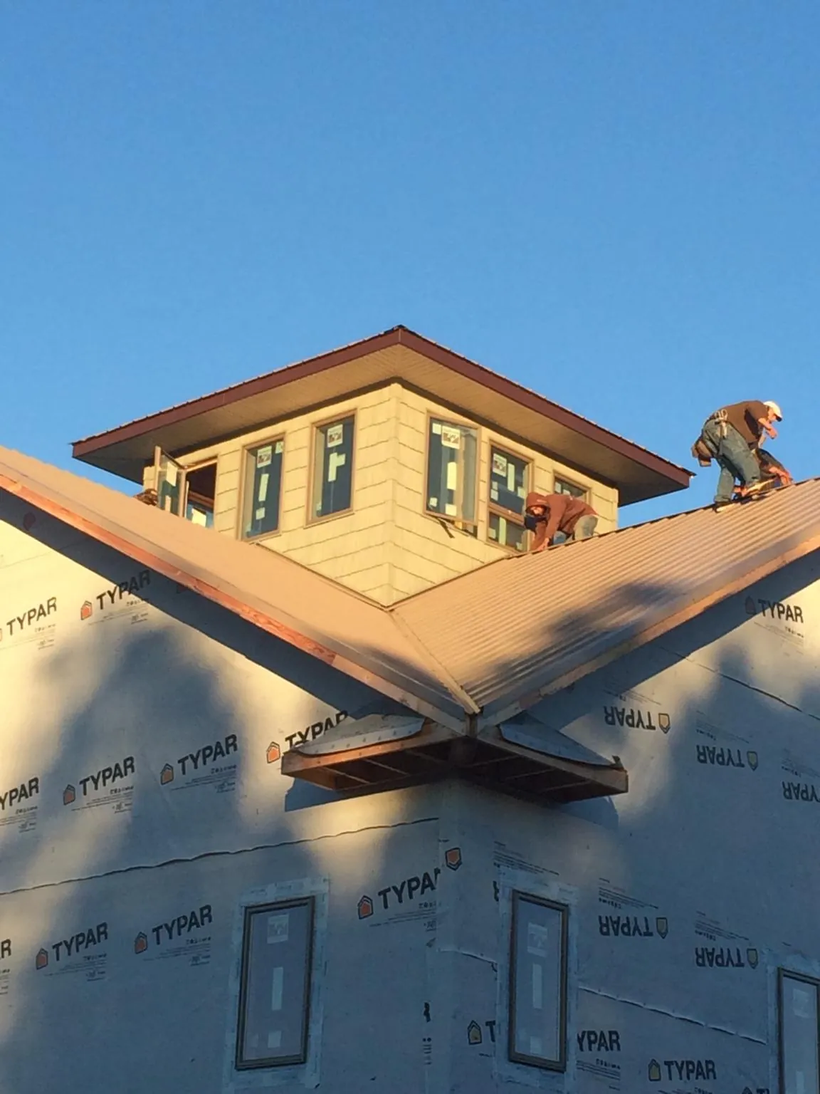 Roofers working around a rooftop cupola on a new metal roof at sunset — Roof Waterproofing in Byron by Roofing Brothers